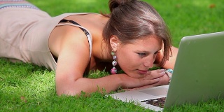 微笑的学生躺在草地上看笔记本电脑