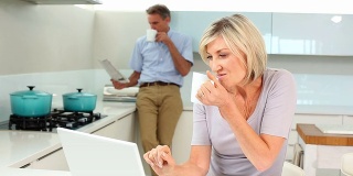 一个女人在用笔记本电脑，而她的丈夫正在看报纸