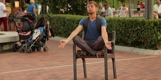 一个滑稽的人在公园的椅子上莲花坐姿冥想，