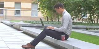 在户外，阳台上，喝着咖啡，用笔记本电脑工作的时尚男士