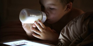 男孩喝着奶瓶里的牛奶，看着触摸板