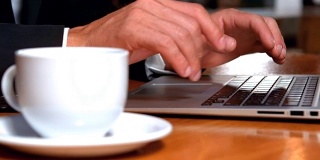 一边喝咖啡一边用笔记本电脑工作的商人