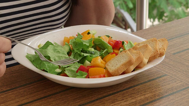 女人在外面吃清淡的午餐，在阳台上吃新鲜的蔬菜沙拉