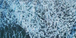 无人机拍摄的巨浪冲上海岸的画面。海啸冲击海滩的封锁镜头。当强大的海浪撞击时，白色的海洋泡沫产生了纹理。这段视频是从头顶的角度拍摄的。