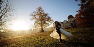 一对夫妇在日落时跳舞。新郎举起新娘，用慢镜头拉近她的镜头