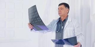 医生在看放射照片的肖像。年长的教授看着分析在白人现代诊所