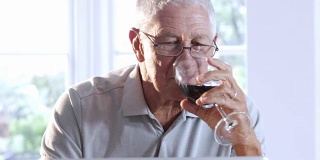 用笔记本电脑和喝红酒的老人