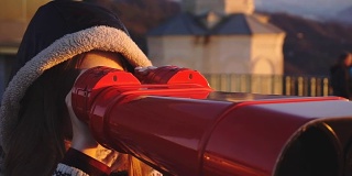 游客通过投币式双筒望远镜在日落时观看城市，特写