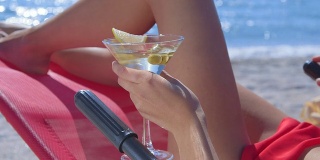 女性手握马提尼与橄榄在热带海滩上的特写