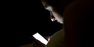 年轻人晚上在床上盖着毯子使用智能手机