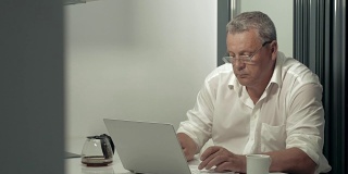 一个严肃的成年人一边在厨房喝咖啡一边用笔记本电脑工作