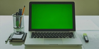 绿色屏幕的笔记本电脑在办公室的现代玻璃桌上摆放4K