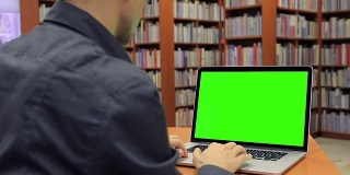 年轻帅哥坐在图书馆的绿屏笔记本电脑上工作