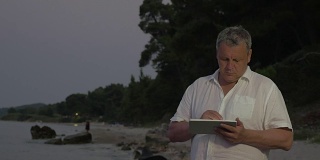 深夜在海滩上用平板电脑的老人