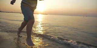 Barefoot kid running in sea water at sunset