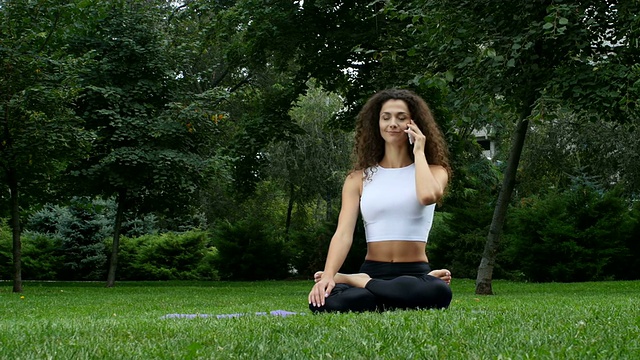 年轻女子在公园里练瑜伽，一边讲电话
