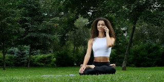 年轻女子在公园里练瑜伽，一边讲电话