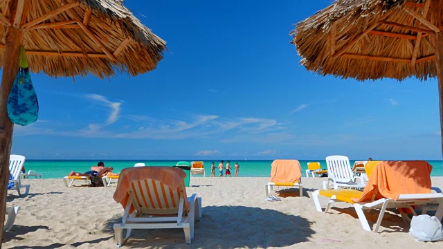 游客在热带海滩上的茅草伞下休息。