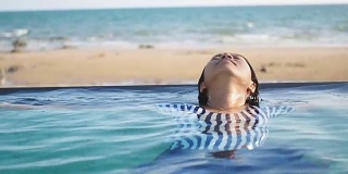 女子在游泳池里放松，背景是大海风光。