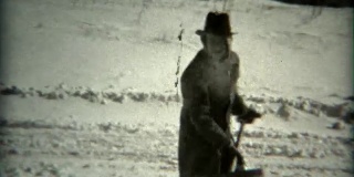 1936年:一名头戴软呢帽、头上裹着围巾的男子在镜头前铲雪。