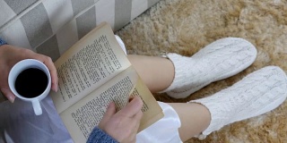 一个穿着睡衣的女人正在家里看书，桌上放着一杯咖啡和一部手机
