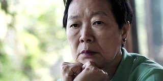 视频中亚洲资深女性手放在脸上思考，担心和悲伤