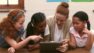 微笑的老师和学生在教室里使用平板电脑视频素材模板下载