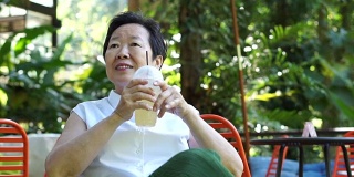 亚洲资深妇女喝咖啡快乐在绿色葱郁的自然咖啡店