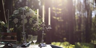 近距离的白色复古烛台上的婚礼装饰表在森林。背景是一束白玫瑰。森林里的浪漫晚餐