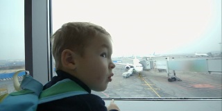 小男孩望着窗外，指着飞机