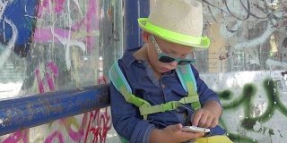 一个男孩在肮脏的城市公交站拿着智能手机