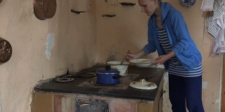 女人在厨房泥炉里用勺子从锅里拿食物。