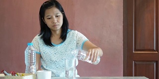 亚洲妇女把水从瓶子倒到玻璃杯里然后喝。