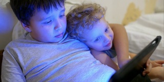 两个男孩在床上拿着触摸板。一个玩游戏