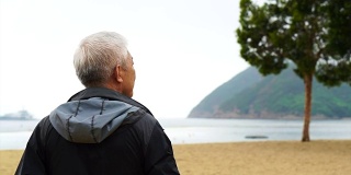 一个亚洲老人独自站在海滩前