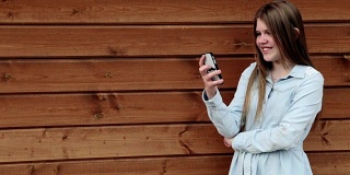 十几岁的女孩抱着她的智能手机在可爱的姿势木制背景拷贝空间