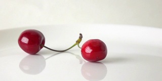 用超级慢镜头拍摄两颗带茎的樱桃撞在白色盘子上