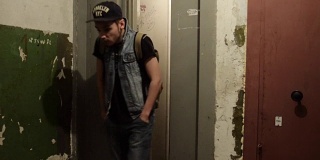 戴着帽子背着背包的男人走出狭窄的电梯。老房子。粗糙的墙壁