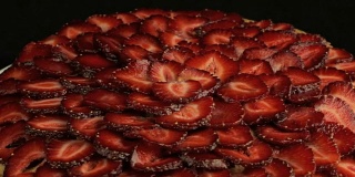 许多红色的草莓被切下，在黑色的背景下缓慢逆时针旋转