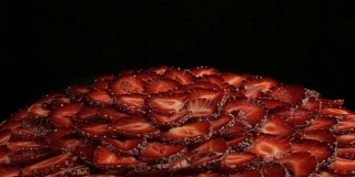 许多美味的红草莓在蛋糕块，缓慢逆时针旋转在黑色的背景