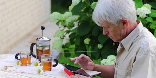 埃尔德曼用数码平板电脑在夏季花园桌上喝茶