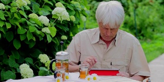 高级男子使用数码平板电脑在夏季花园桌上喝茶