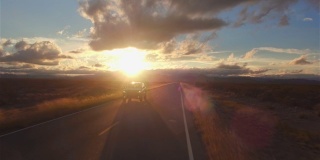 图片:金色的夕阳下，一辆黑色SUV行驶在空旷的乡村道路上