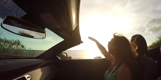 慢镜头:快乐的年轻女子高举双手坐在敞篷车里
