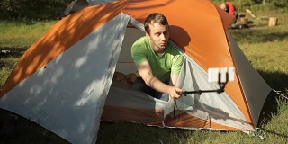 人们在帐篷外通过手机自拍。首先，打开帐篷，拍一张照片，然后关上帐篷。森林里的晴天