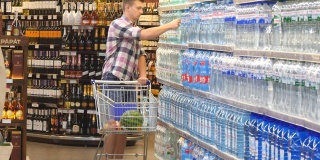 年轻人推着购物车在超市买水。一个人走进商店，拿着产品，一个人在店里买饮料