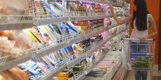 年轻女子推着购物车在超市的冷藏区购买乳制品或冷藏食品。一个女孩走到商店的冰箱前，从里面拿东西