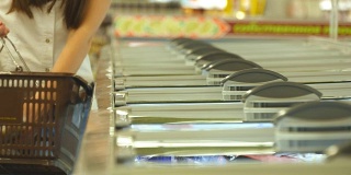 女性双手打开超市冷藏区玻璃门，选择冷藏食品。一名年轻女子在商店从冰箱里拿出产品，并把它放进篮子里