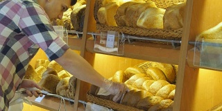 男人在超市里选了一条新鲜的面包。一个年轻人从架子上拿起一块面包闻了闻。在杂货店购物