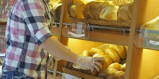 男人在超市里选了一条新鲜的面包。一个年轻人从架子上拿起一块面包闻了闻。在杂货店购物
